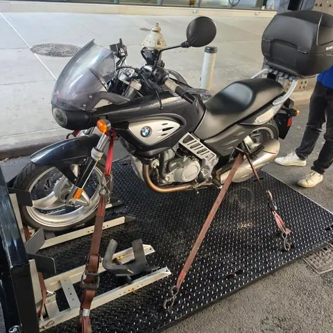 Black and silver BMW motorcycle secured with ratchet straps on the carrier deck