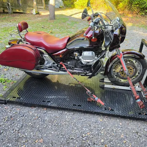Red Moto Guzzi EV1100 strapped down on the carrier deck on a gravel drive