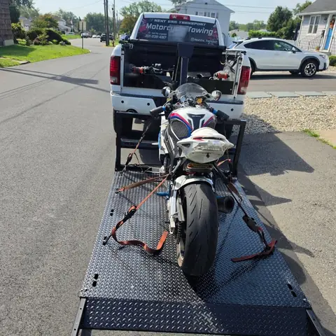 Sport bike secured on the carrier behind the white Next Era Transport pickup truck