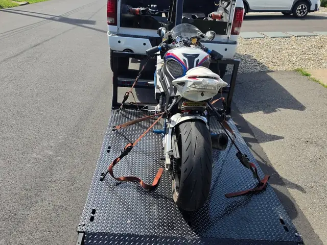 Sport bike secured on the carrier behind the white Next Era Transport pickup truck
