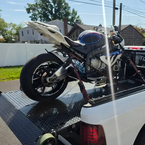 White and blue sport bike strapped down on the carrier behind the pickup truck