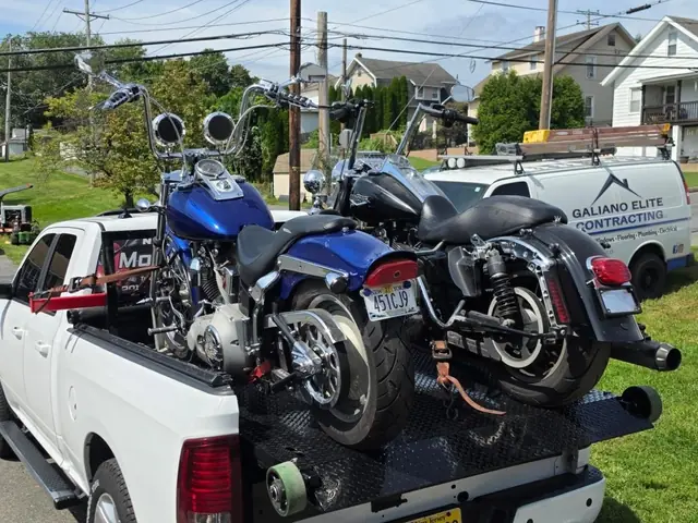 Two Harley-Davidson motorcycles loaded together on the carrier behind a white pickup truck